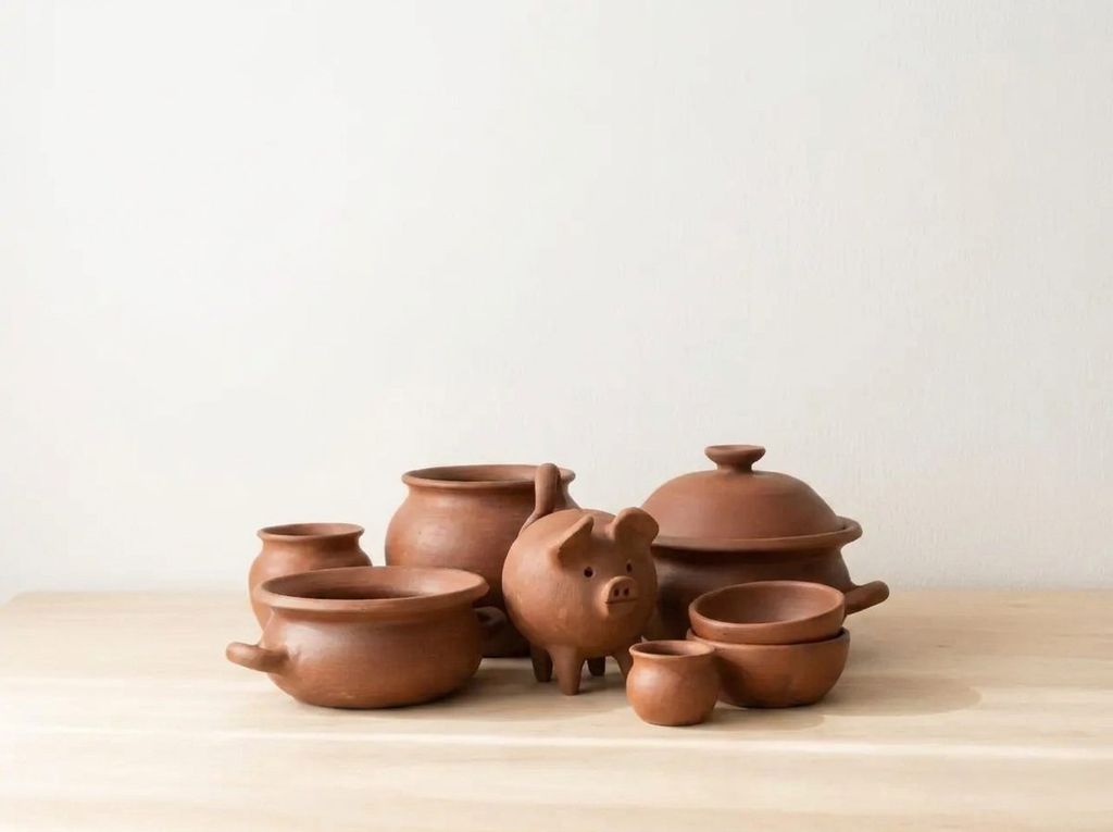 Conjunto de piezas de greda: ollas, cazuela con tapa, chanchito y pocillos sobre madera clara